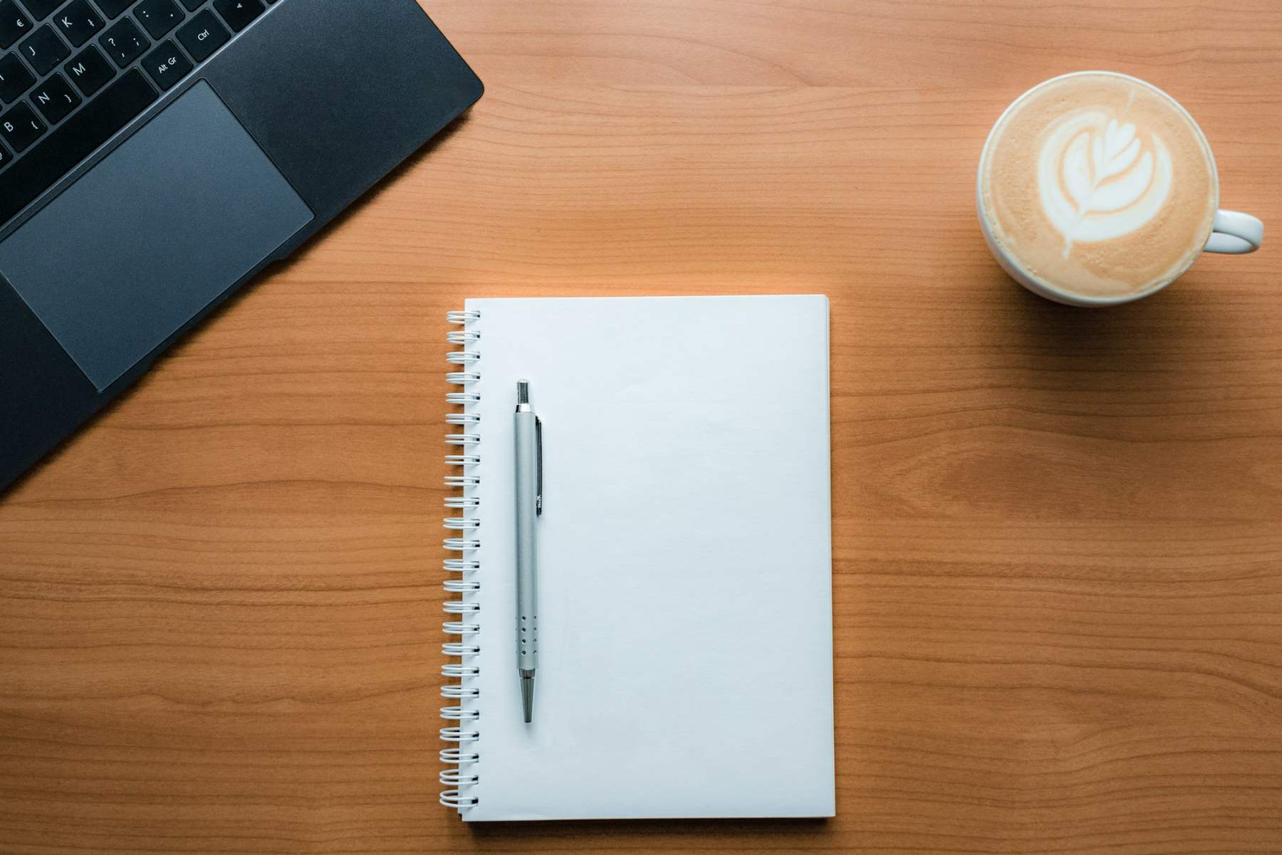 Un cuaderno, un bolígrafo y un café sobre una mesa de madera