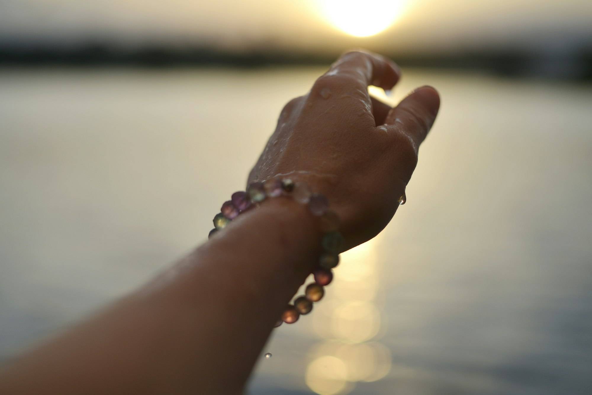 Una muñeca con una pulsera de cuentas, a contraluz del atardecer sobre el agua